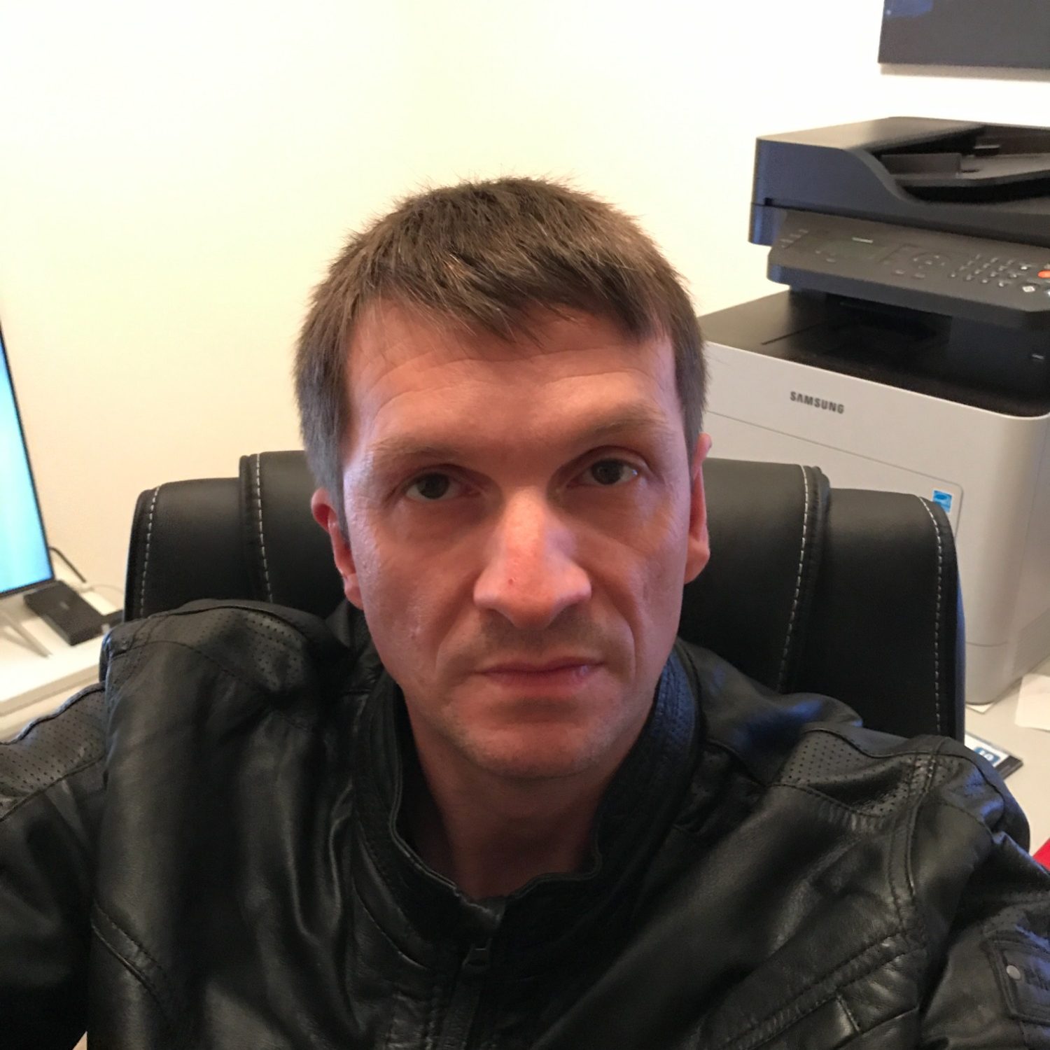 Mann mit kurzem Haar in schwarzer Jacke, sitzt am Schreibtisch vor dem Computer.