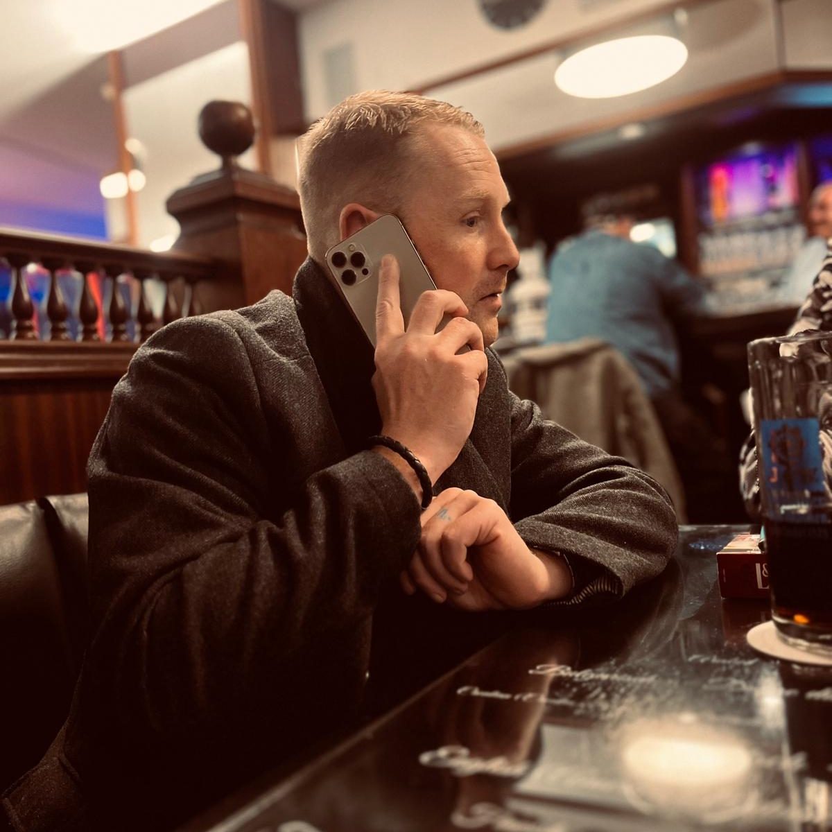 Mann mit Smartphone, sitzt am Tisch in einer Bar und spricht telefonierend.